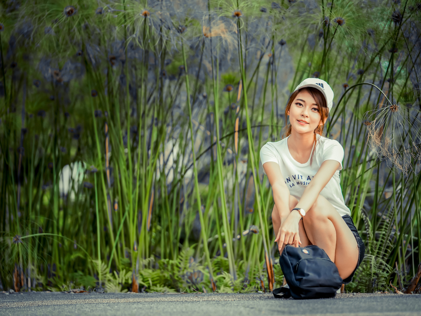 Милая девушка в кепке сидит на дороге с рюкзаком