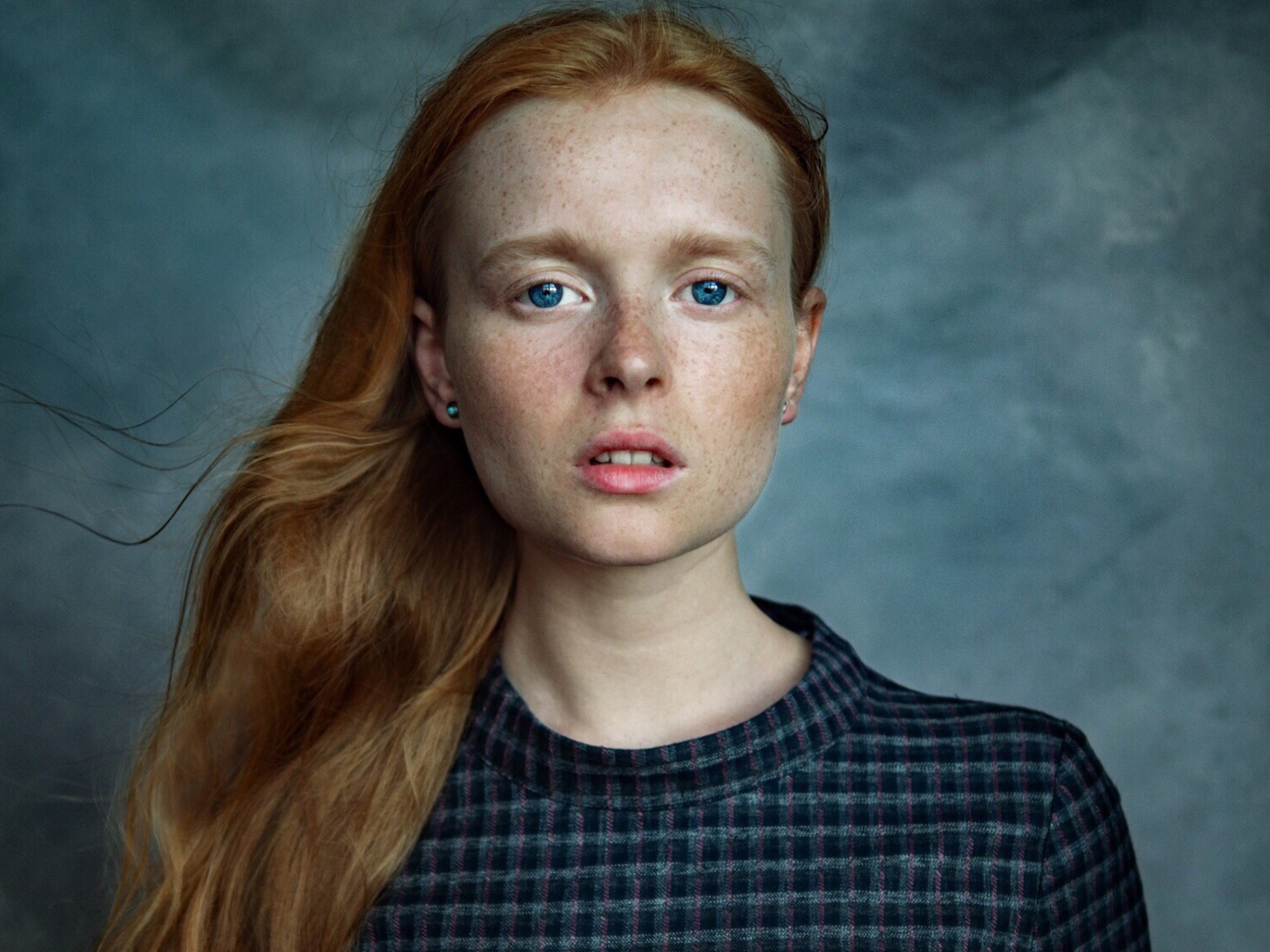 Милая рыжеволосая голубоглазая девушка с веснушками на лице на сером фоне