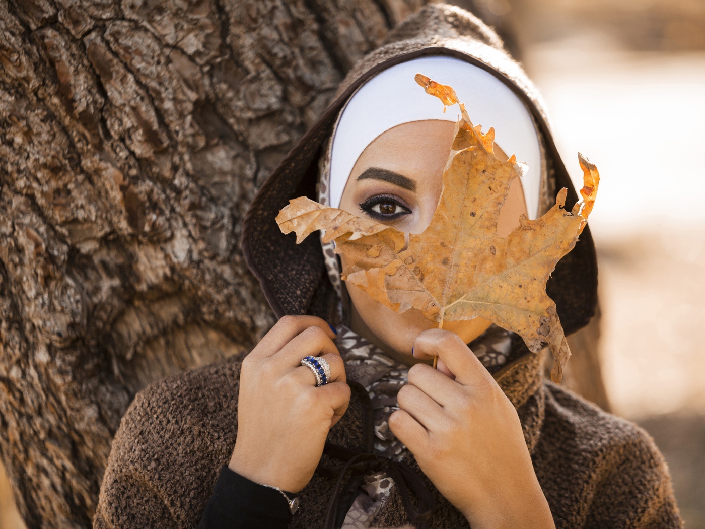 Девушка в пальто с закрывает лицо листом