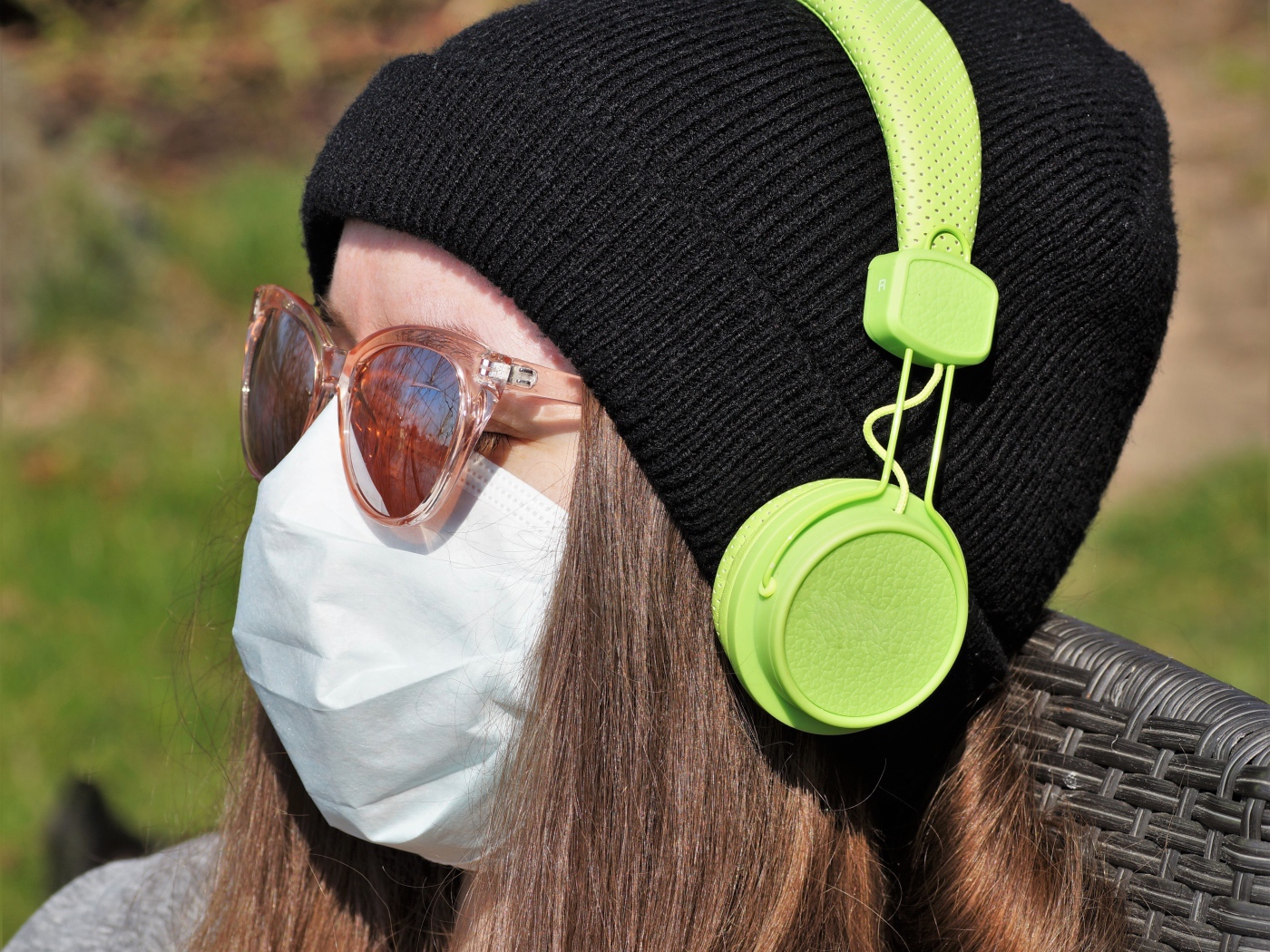 Девушка в медицинской маске на лице, в черной маске и наушниках