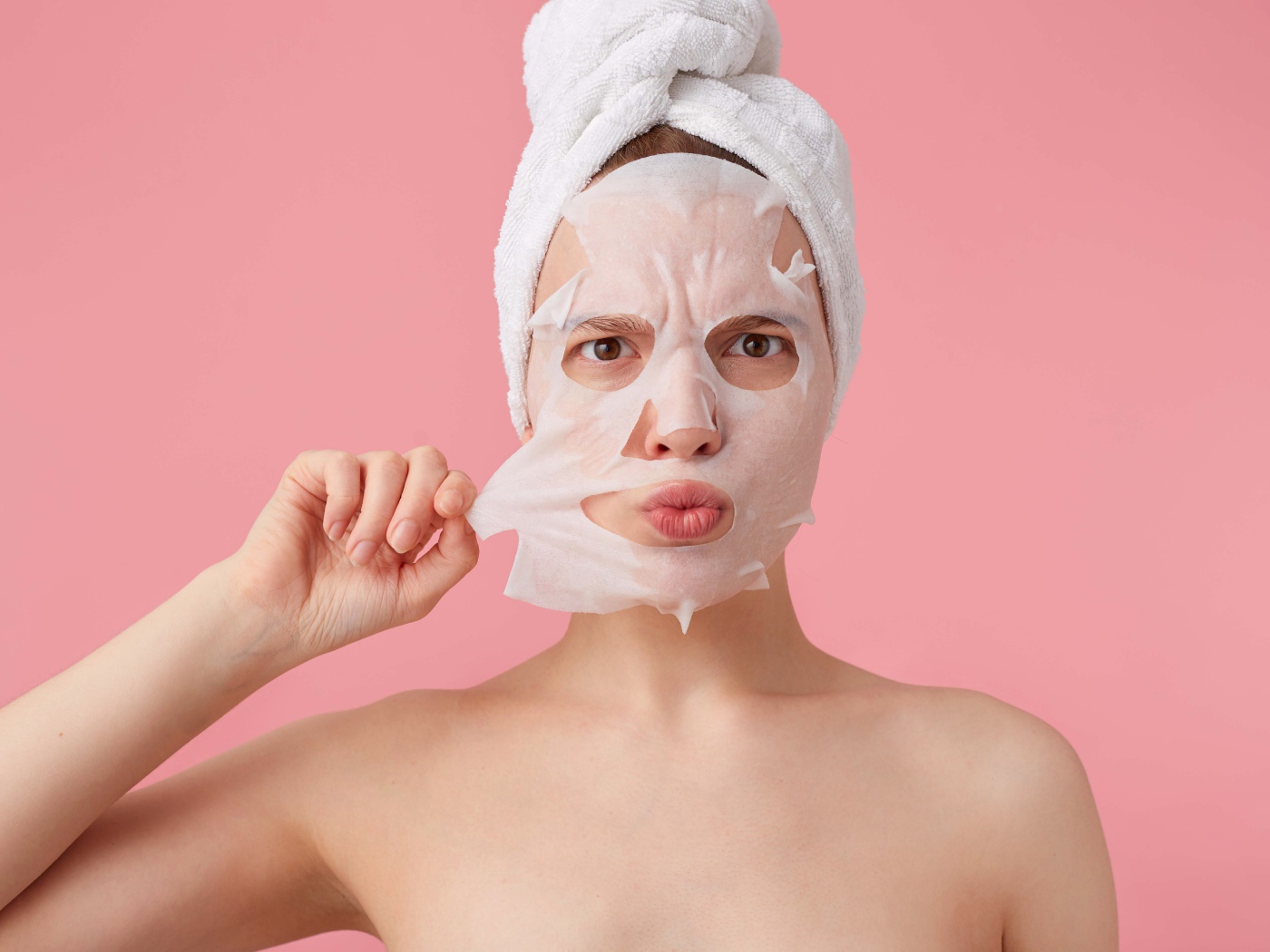 Девушка снимает косметическую маску с лица на розовом фоне 