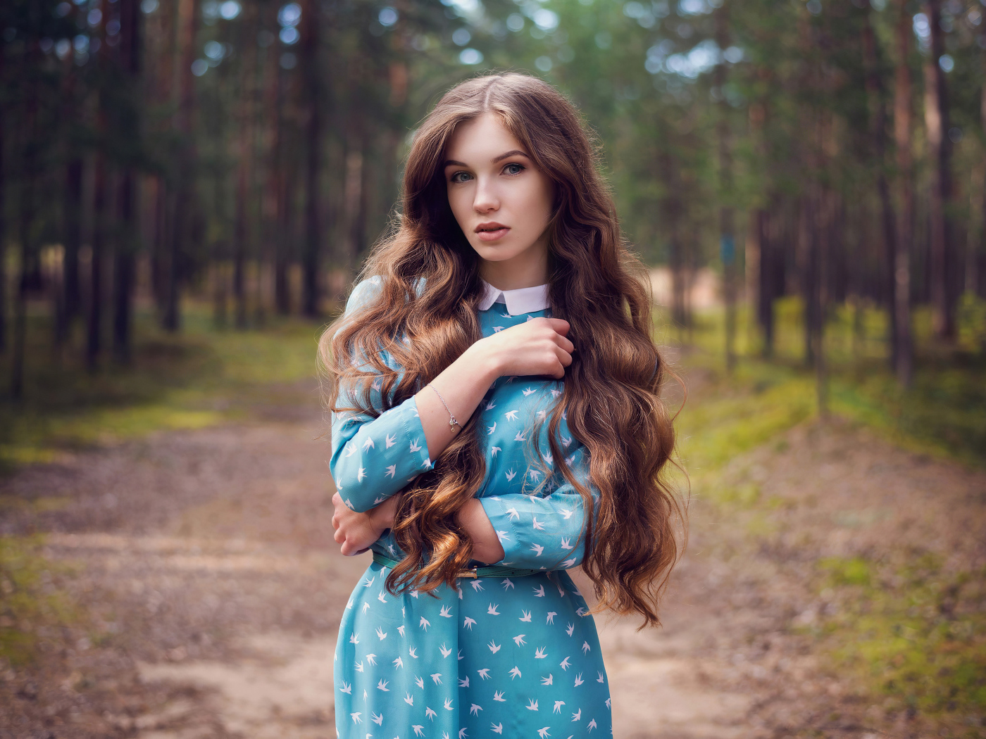 Длинноволосая девушка в голубом платье стоит в лесу