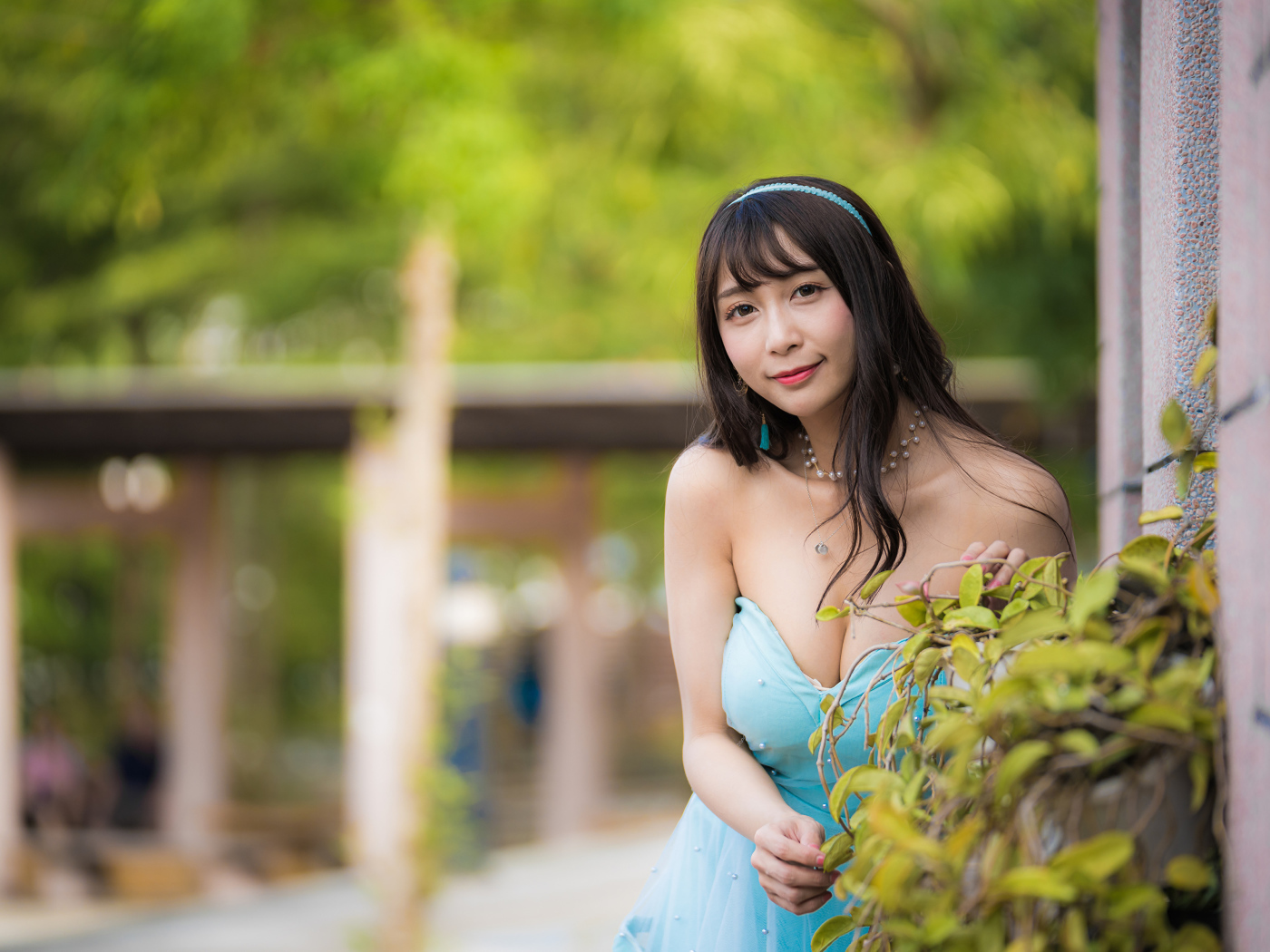 Улыбающаяся девушка азиатка в голубом платье у стены с растением 