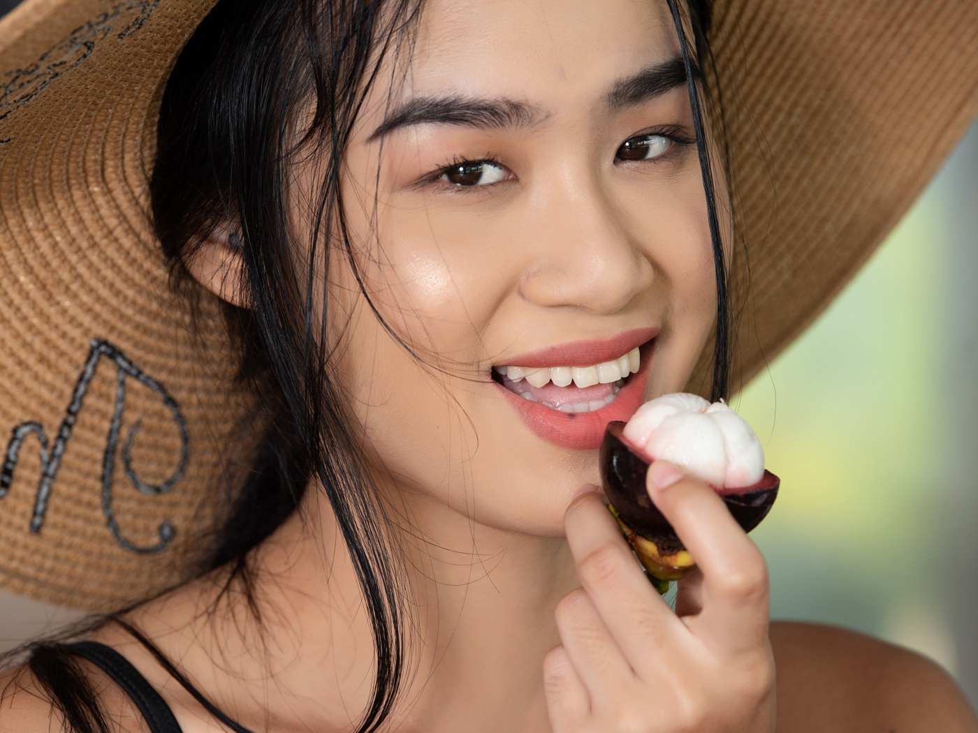Улыбающаяся азиатка в шляпе с фруктом в руке