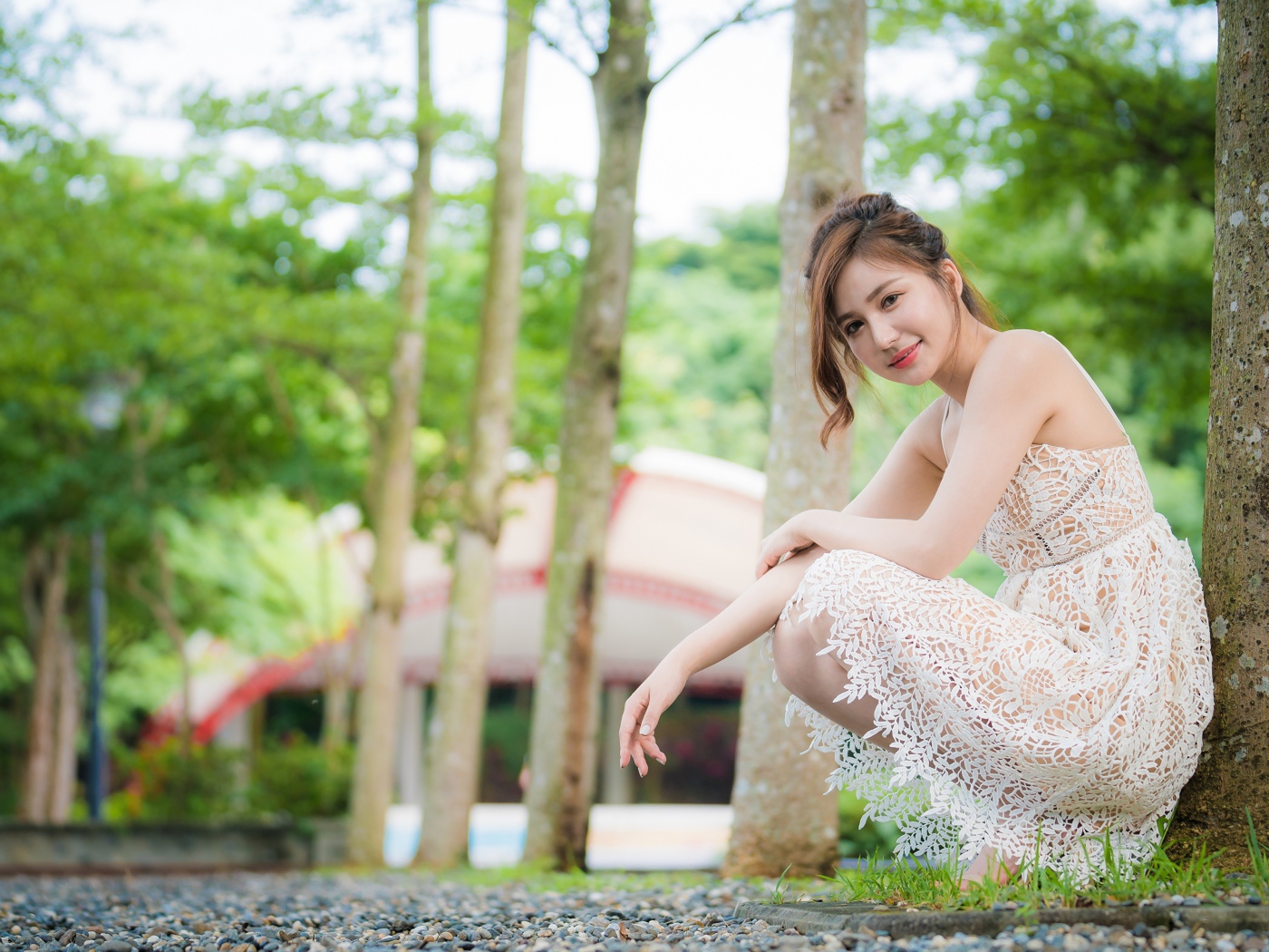 Улыбающаяся девушка в кружевном платье сидит под деревом в парке