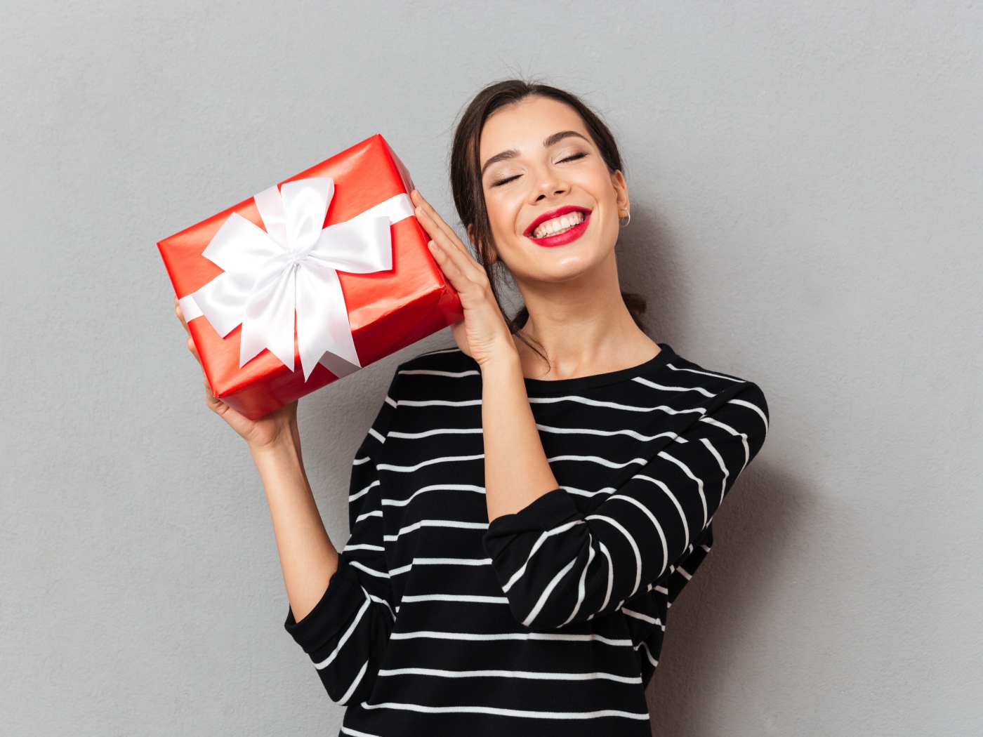Улыбающаяся девушка с подарком в руках на сером фоне 