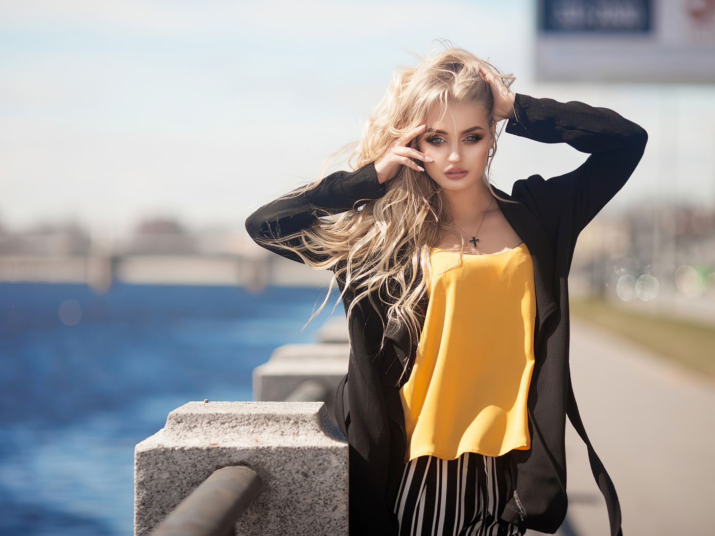 Эффектная блондинка в черном пальто стоит у воды