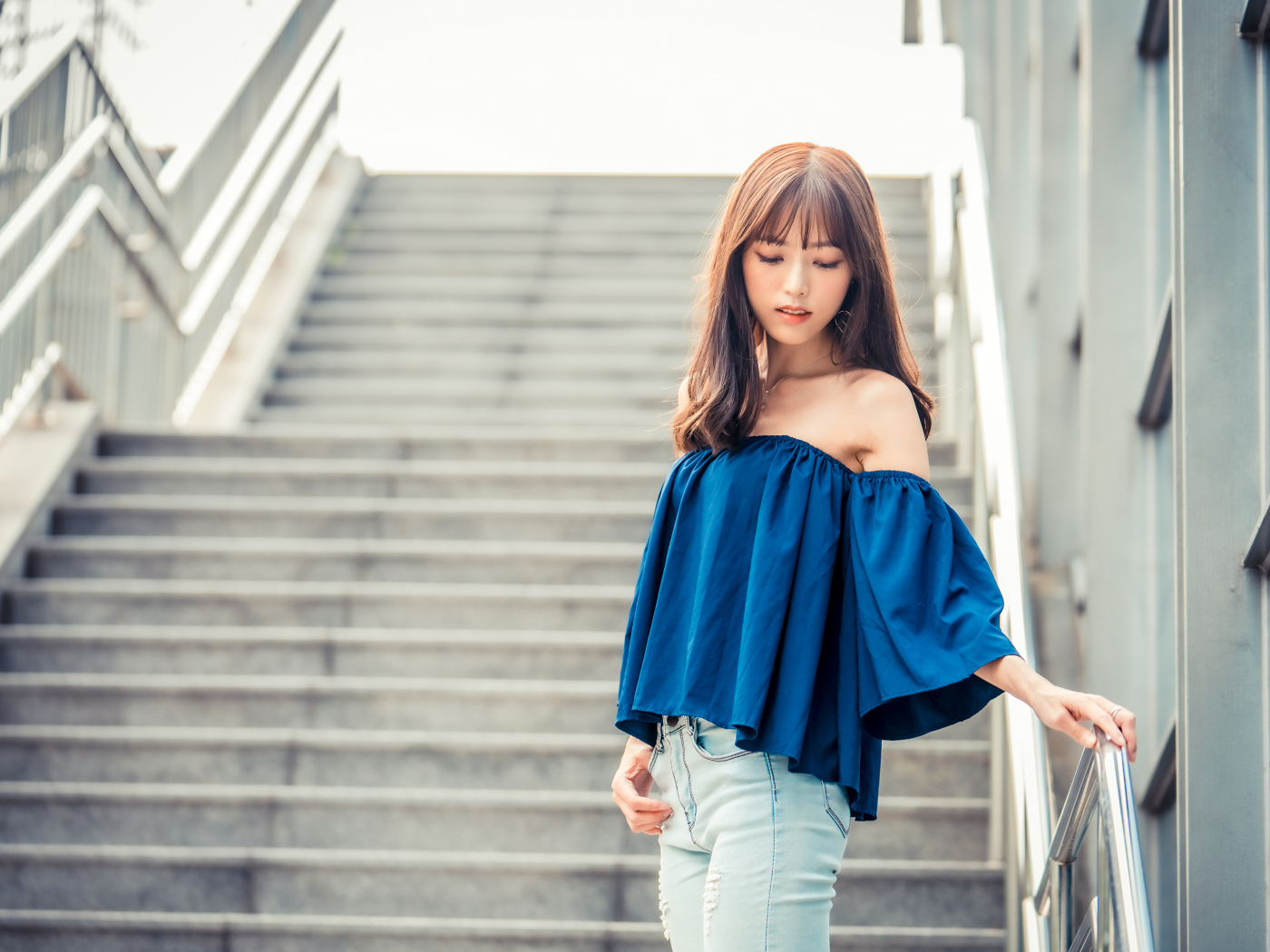 Стильная девушка азиатка с опущенной головой стоит на ступеньках 