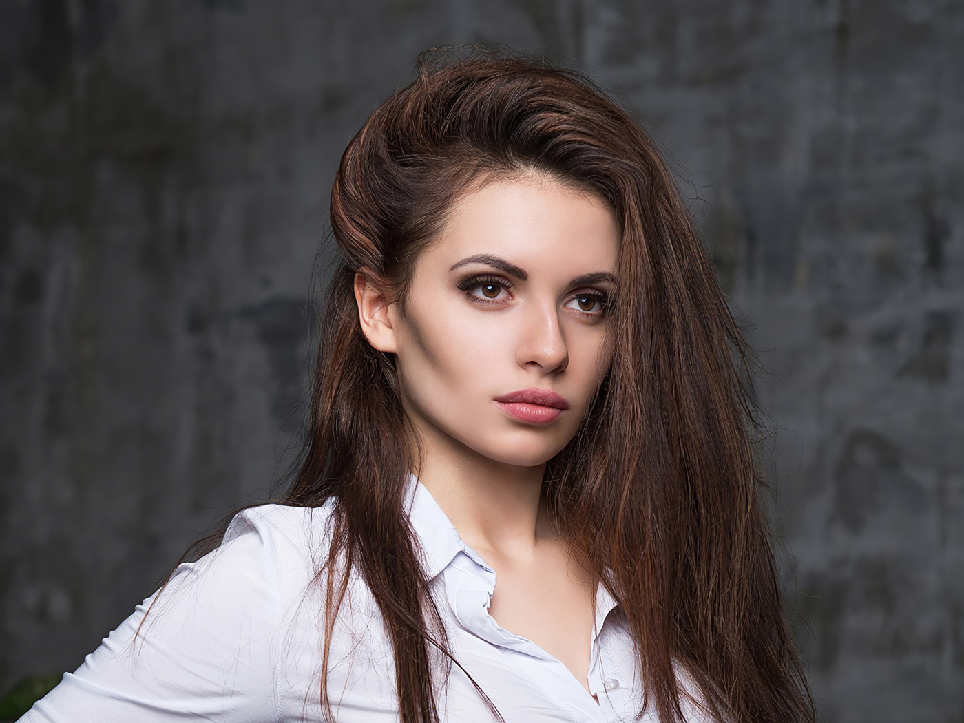 Стильная девушка в белой рубашке на фоне серой стены 