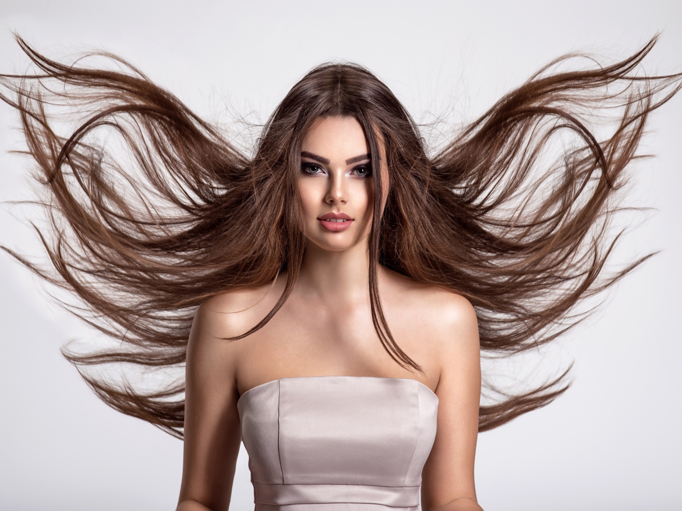 Ветер развивает волосы красивой девушке шатенке на сером фоне