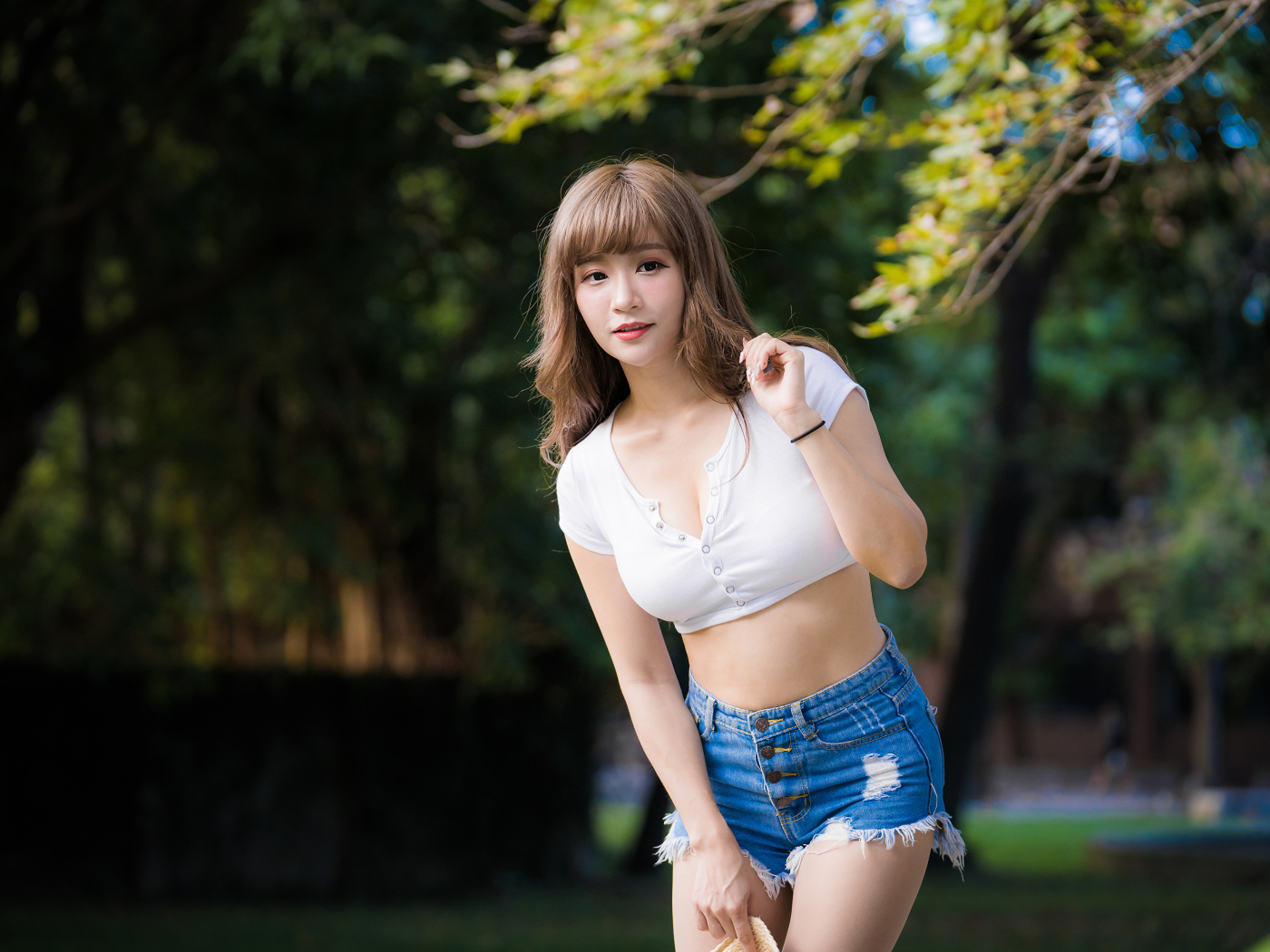 Молодая азиатка в белом топе и синих шортах  в парке