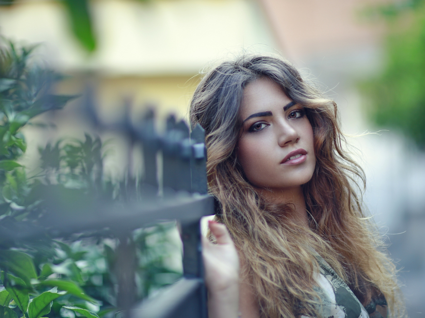 Молодая девушка с длинными волосами стоит у забора