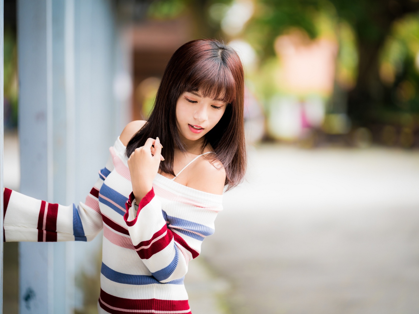 Молодая нежная девушка азиатка в свитере стоит у забора 