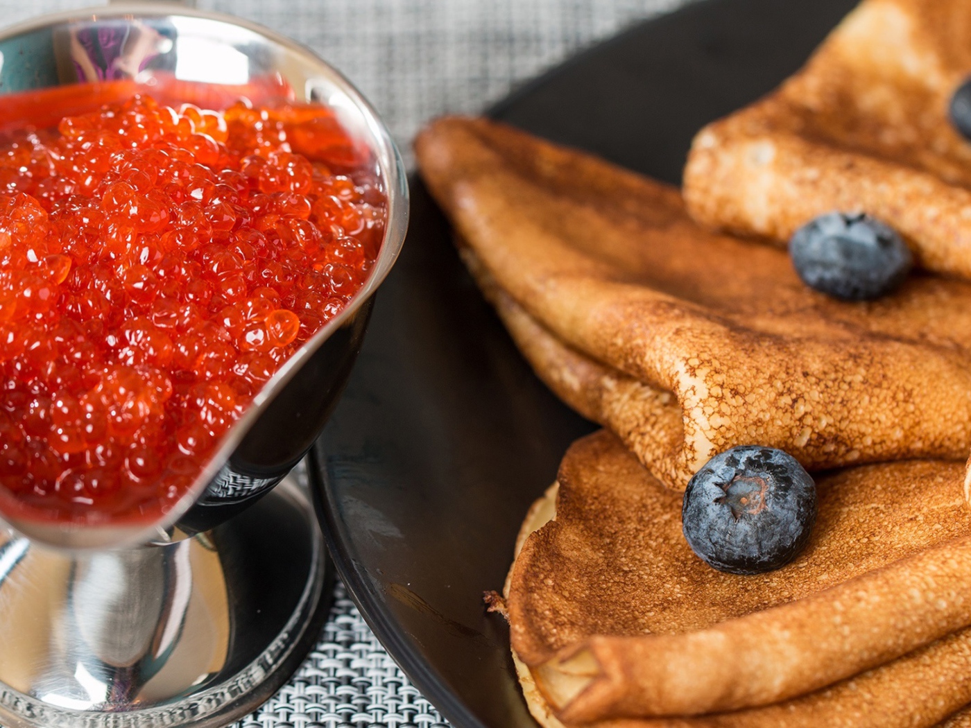 Тонкие блины с ягодами черники на столе с красной икрой на Масленицу