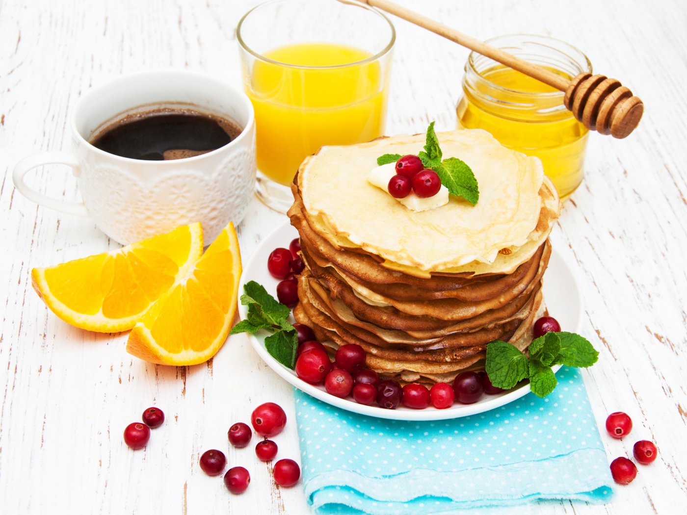 Тонкие румяные блинчики на столе с ягодами клюквы, апельсинами, медом и кофе