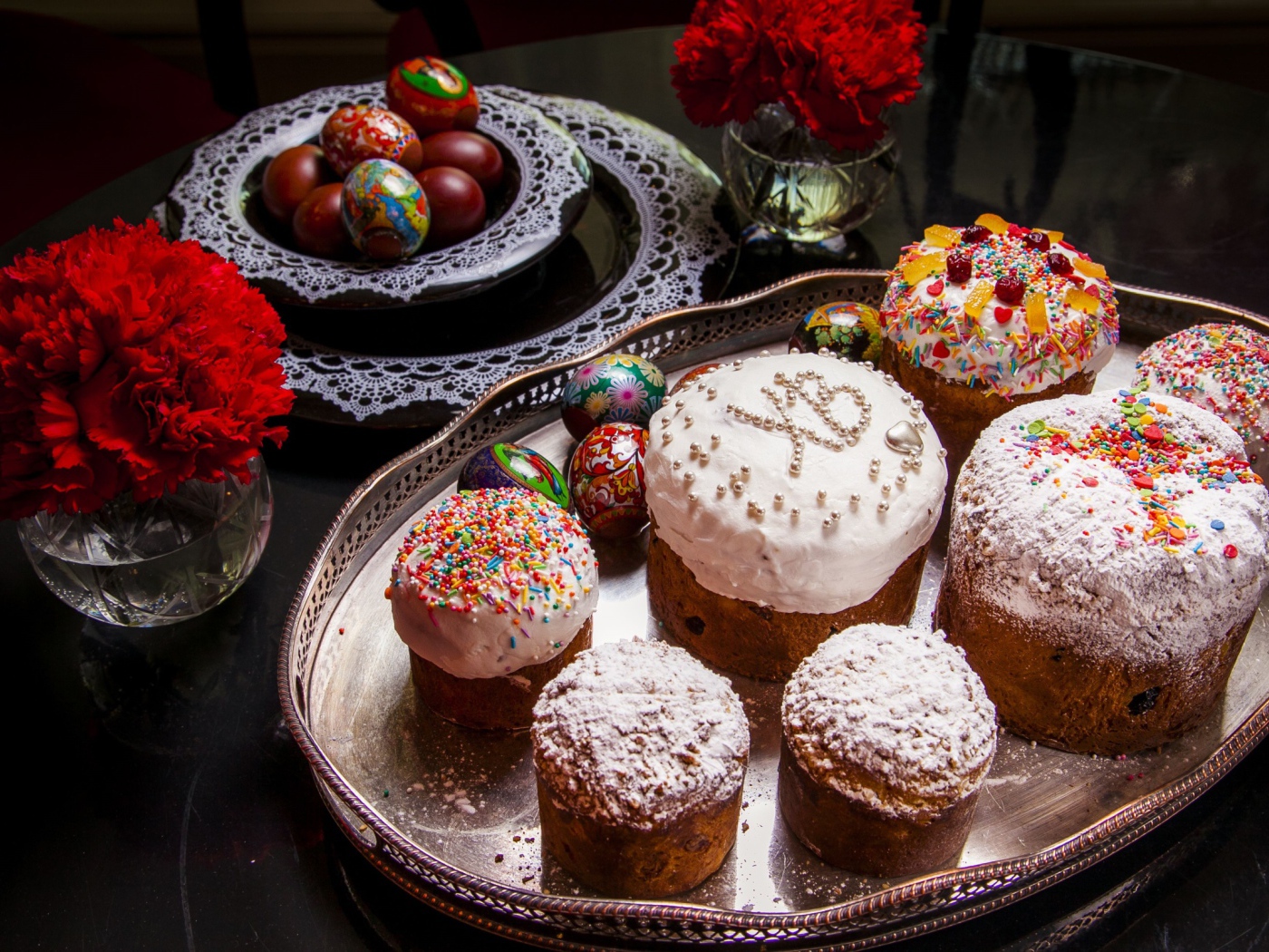 Много куличей на столе с гвоздиками и крашеными яйцами на праздник Пасха