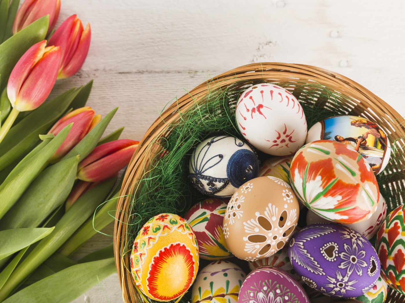 Разноцветные крашеные яйца в корзине с букетом тюльпанов на Пасху