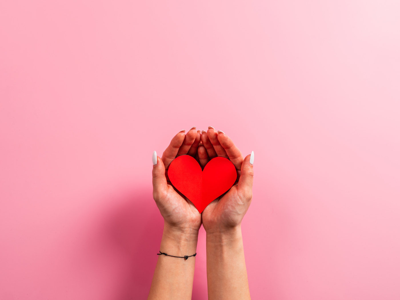 Красное бумажное сердце в руках на розовом фоне
