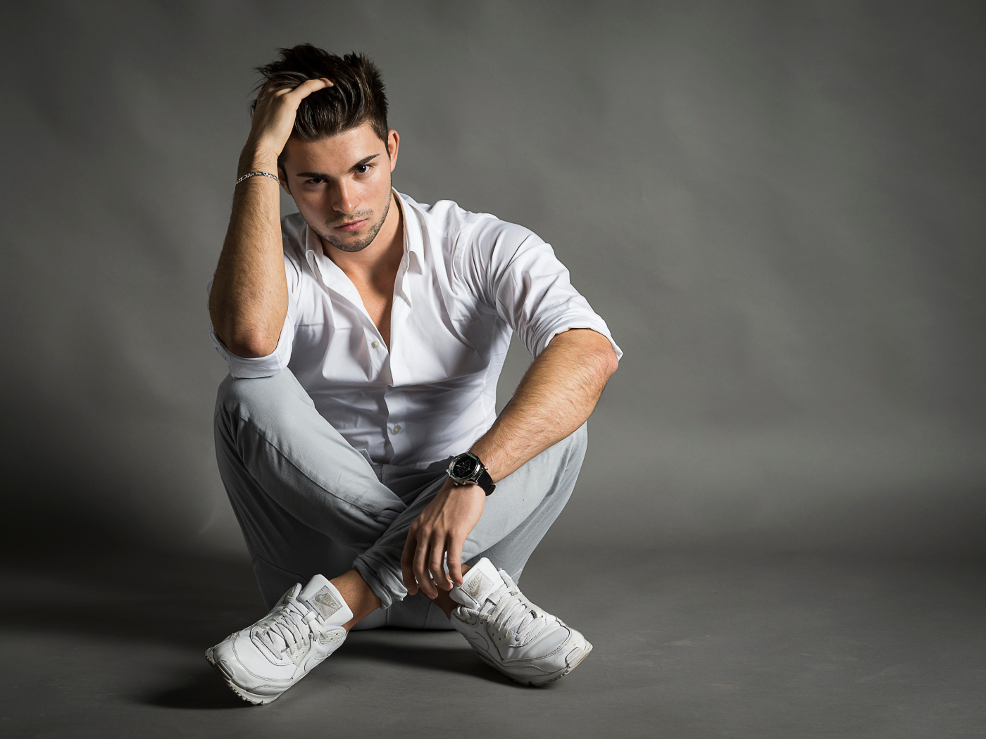 Handsome young man in white shirt sits by the wall