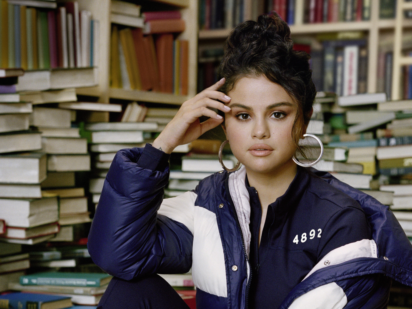 Актриса и певица Селена Гомес в куртке сидит в библиотеке