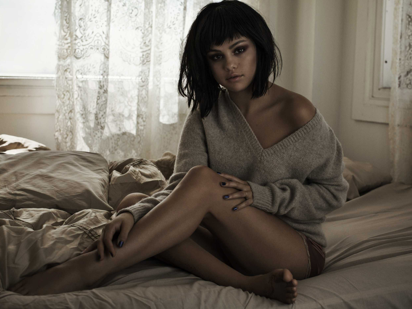 Певица Селена Гомес сидит в свитере на кровати