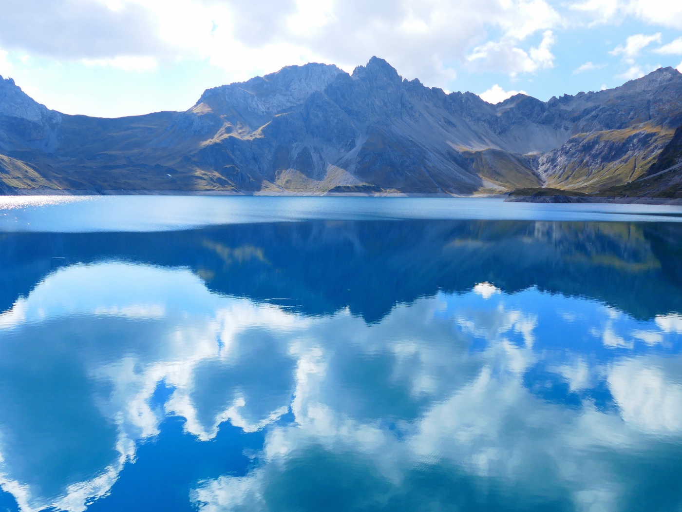 Beautiful white clouds are reflected in the water of the lake against the background of mountains