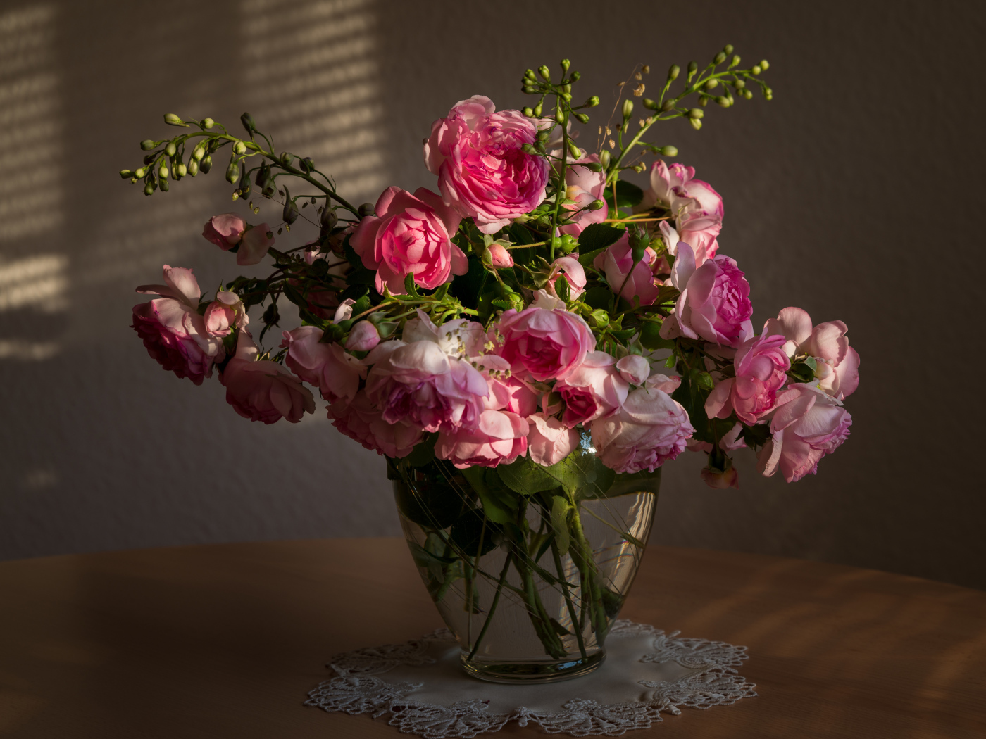 Букет розовых роз в стеклянной вазе не столе в лучах солнца 