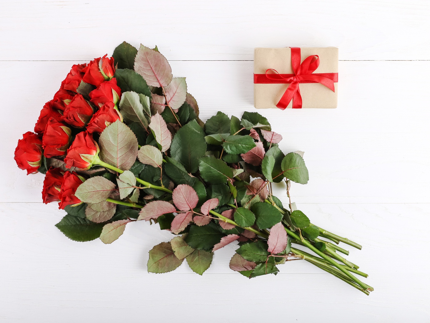 Букет колючих красных роз с подарком на белом фоне