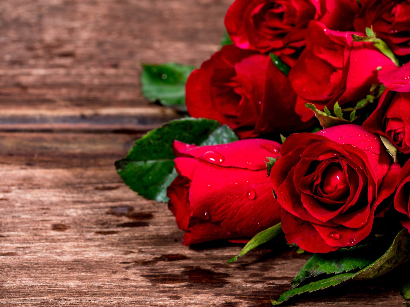 Букет красных роз на деревянном столе в каплях воды