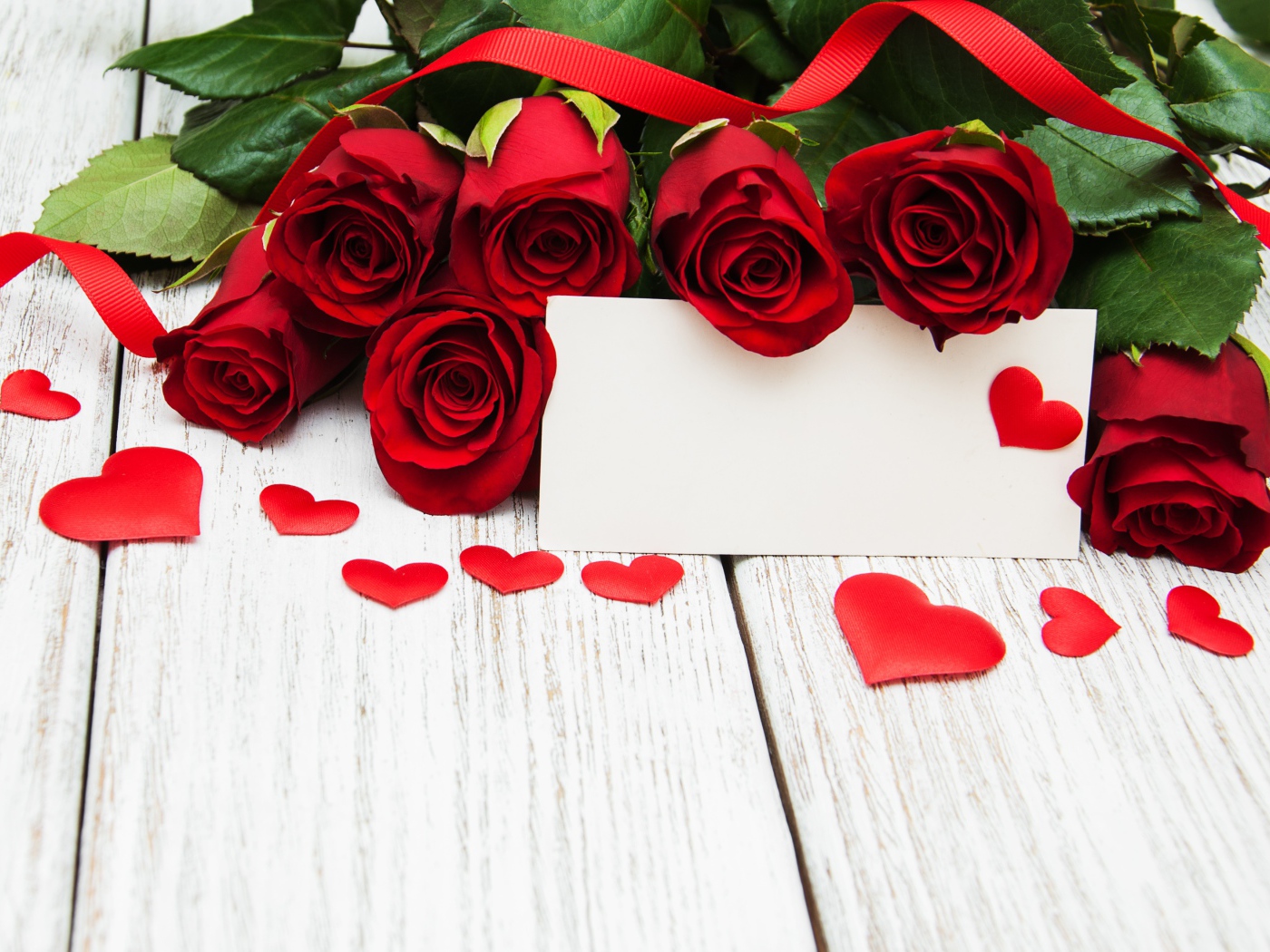 Букет красных роз на столе с сердечками и открыткой