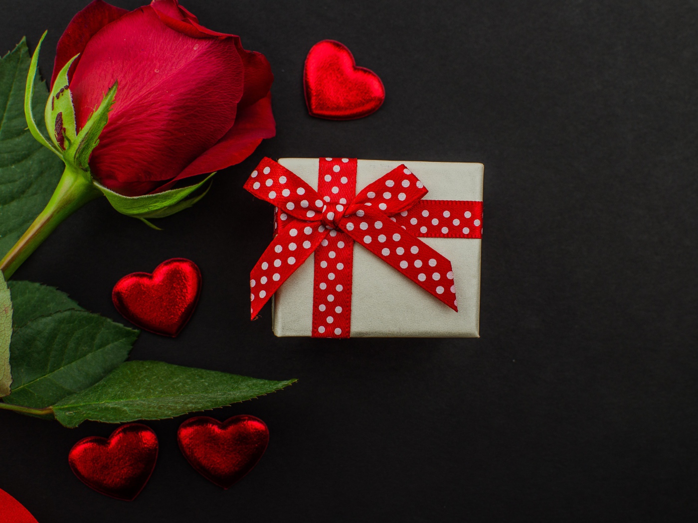 Маленький подарок и красная роза на черном столе