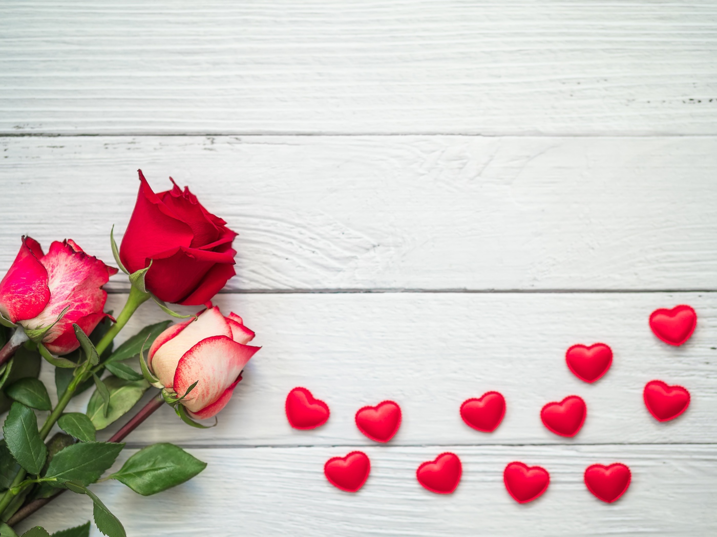 Три свежие розы на сером столе с красными сердечками