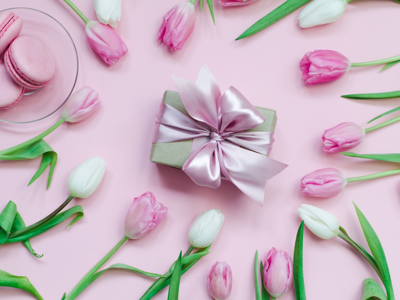 Тюльпаны на розовом фоне с подарком и десертом макарон 
