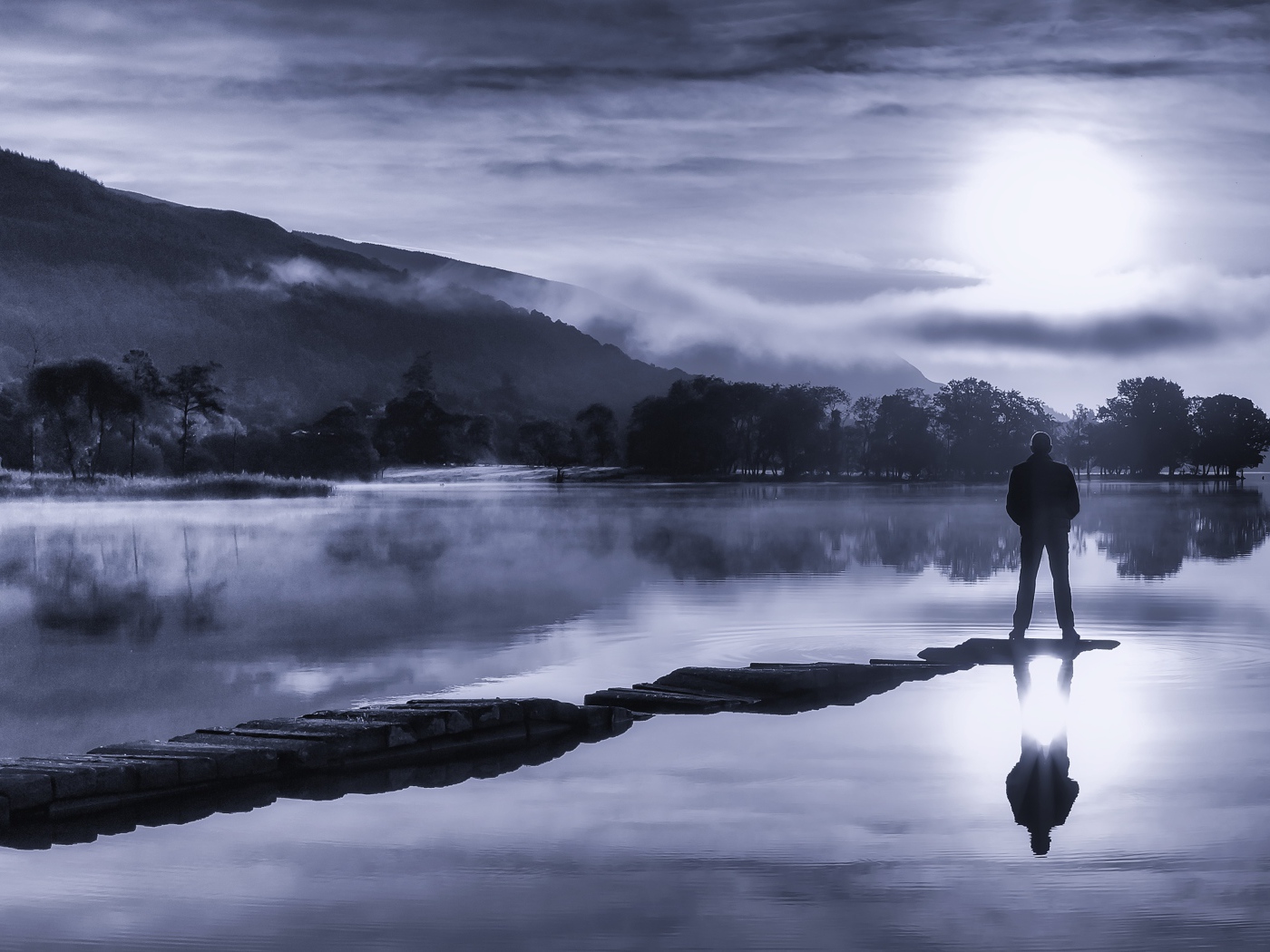 Мужчина стоит на мосту у озера ночью при свете луны