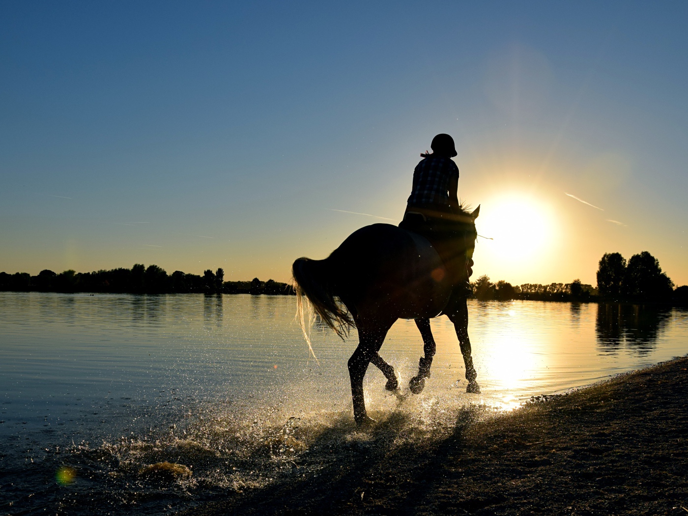 Девушка на лошади скачет по воде на закате солнца