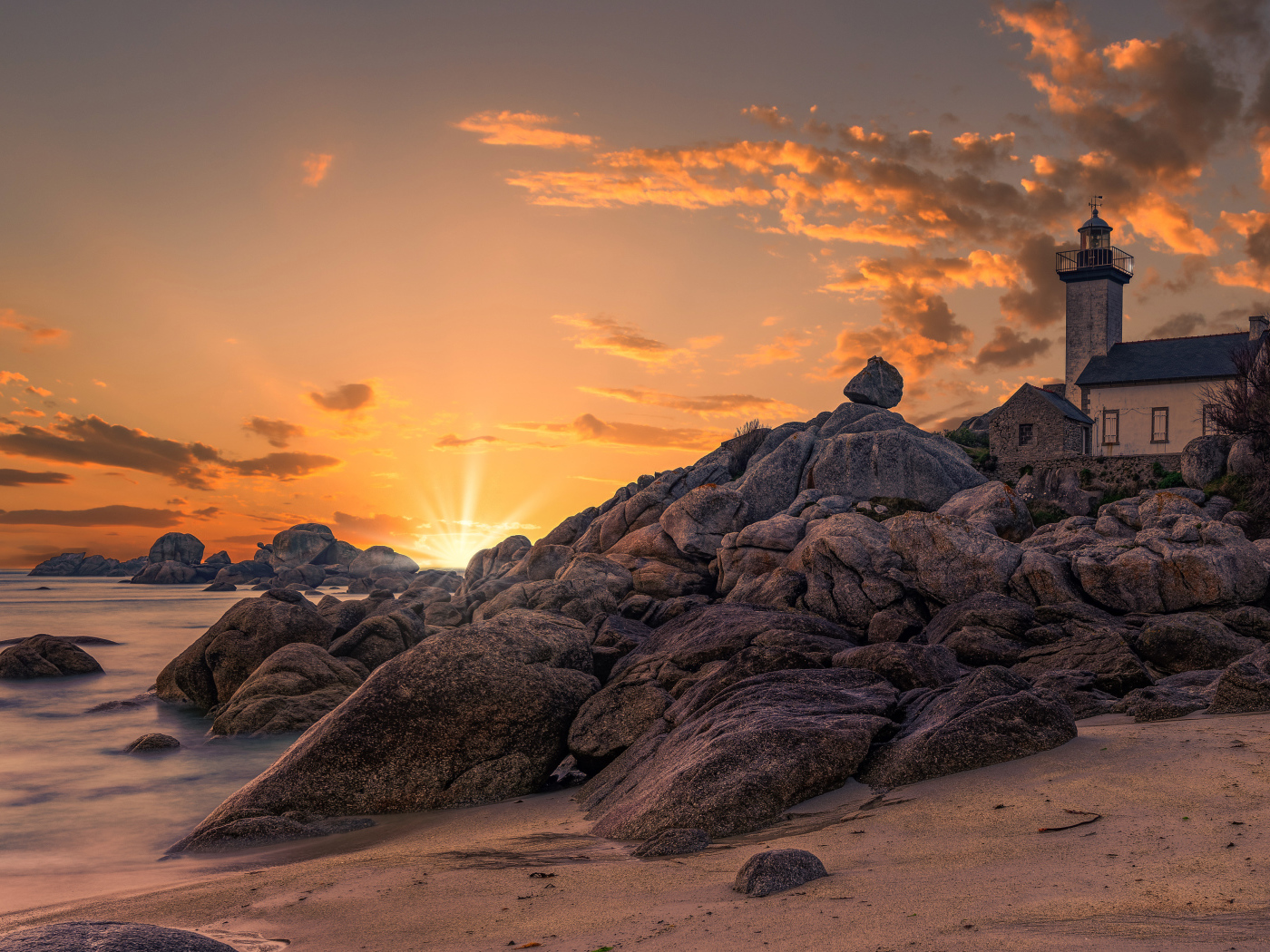 Lighthouse on the shore of a stone shore at sunset