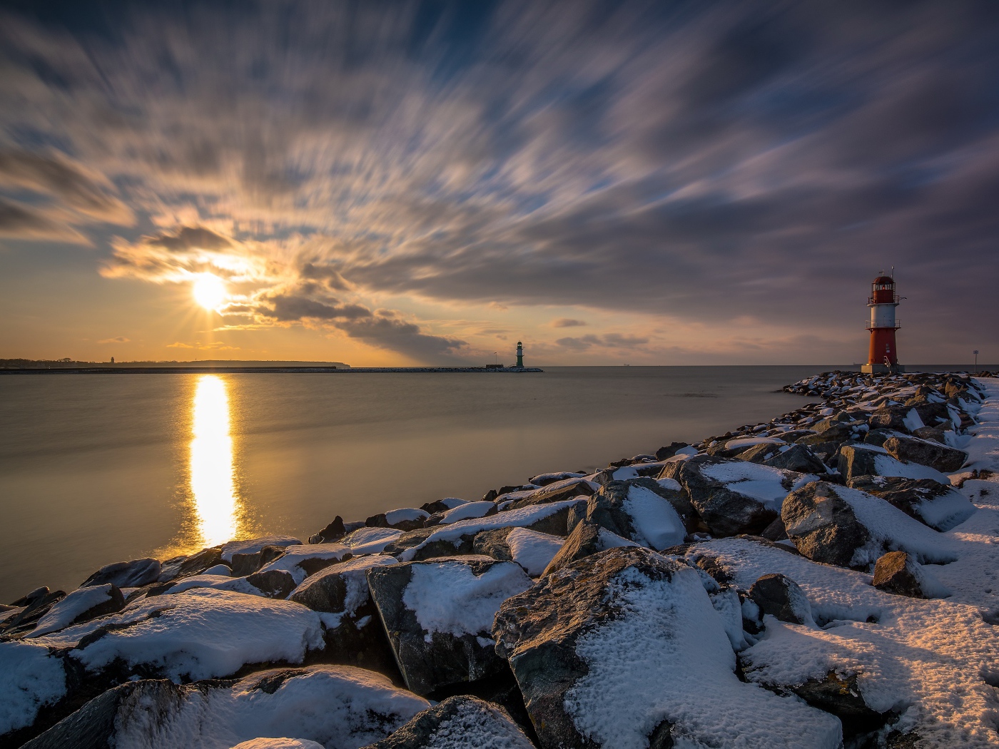 Заснеженные камни на берегу моря с маяком на закате