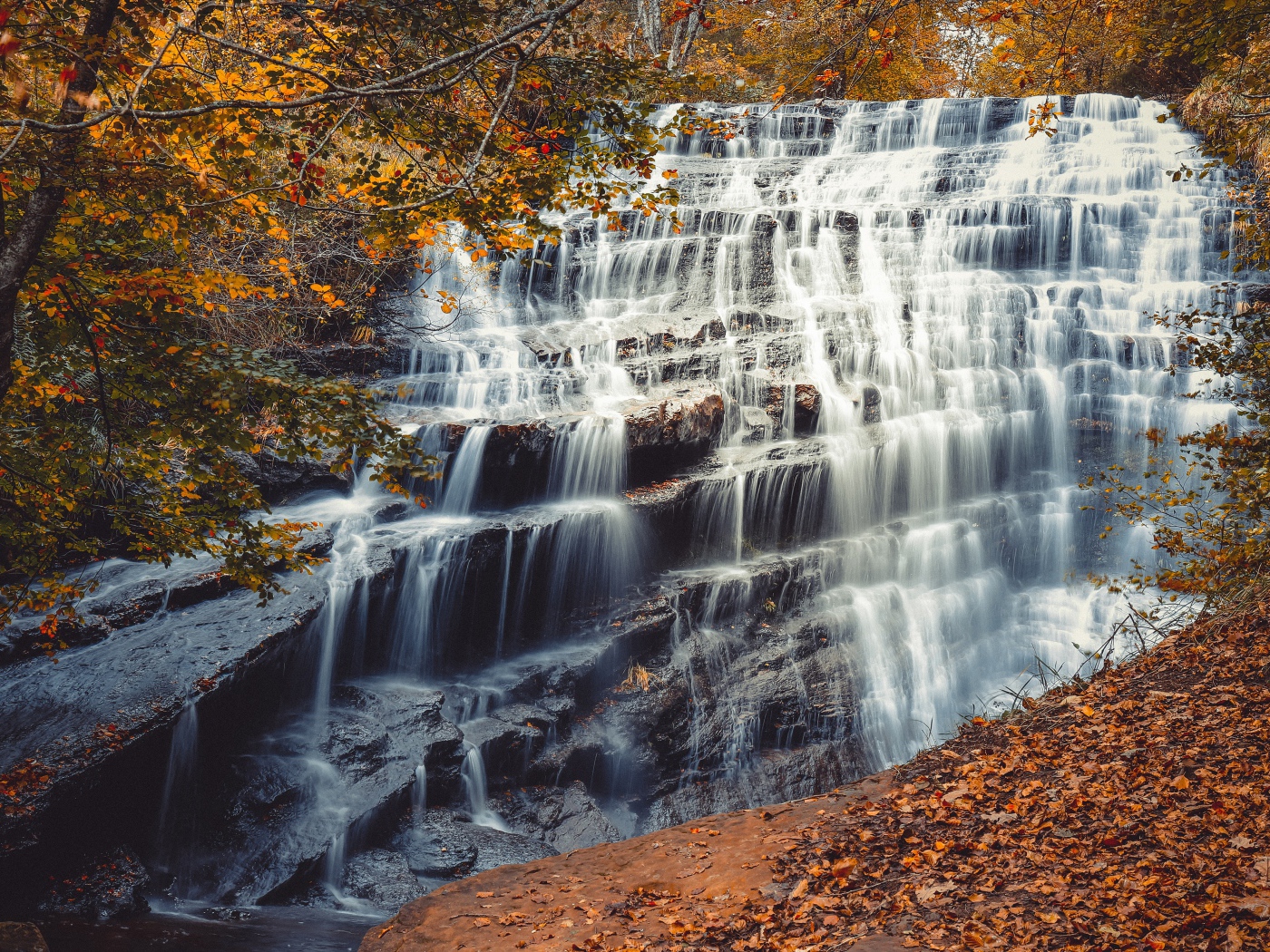 Быстрая вода водопада стекает по каскадам камней осенью