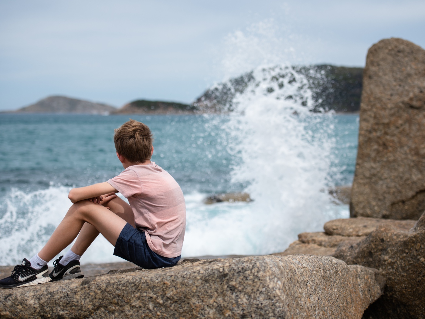 Мальчик сидит на камнях у бушующего моря