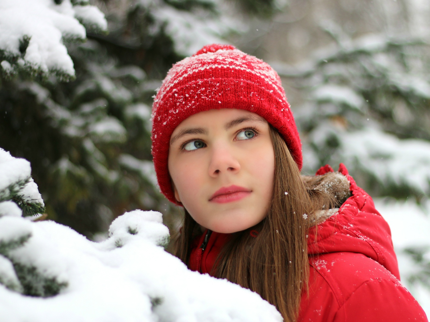 Милая девочка в красной шапке у заснеженной ели