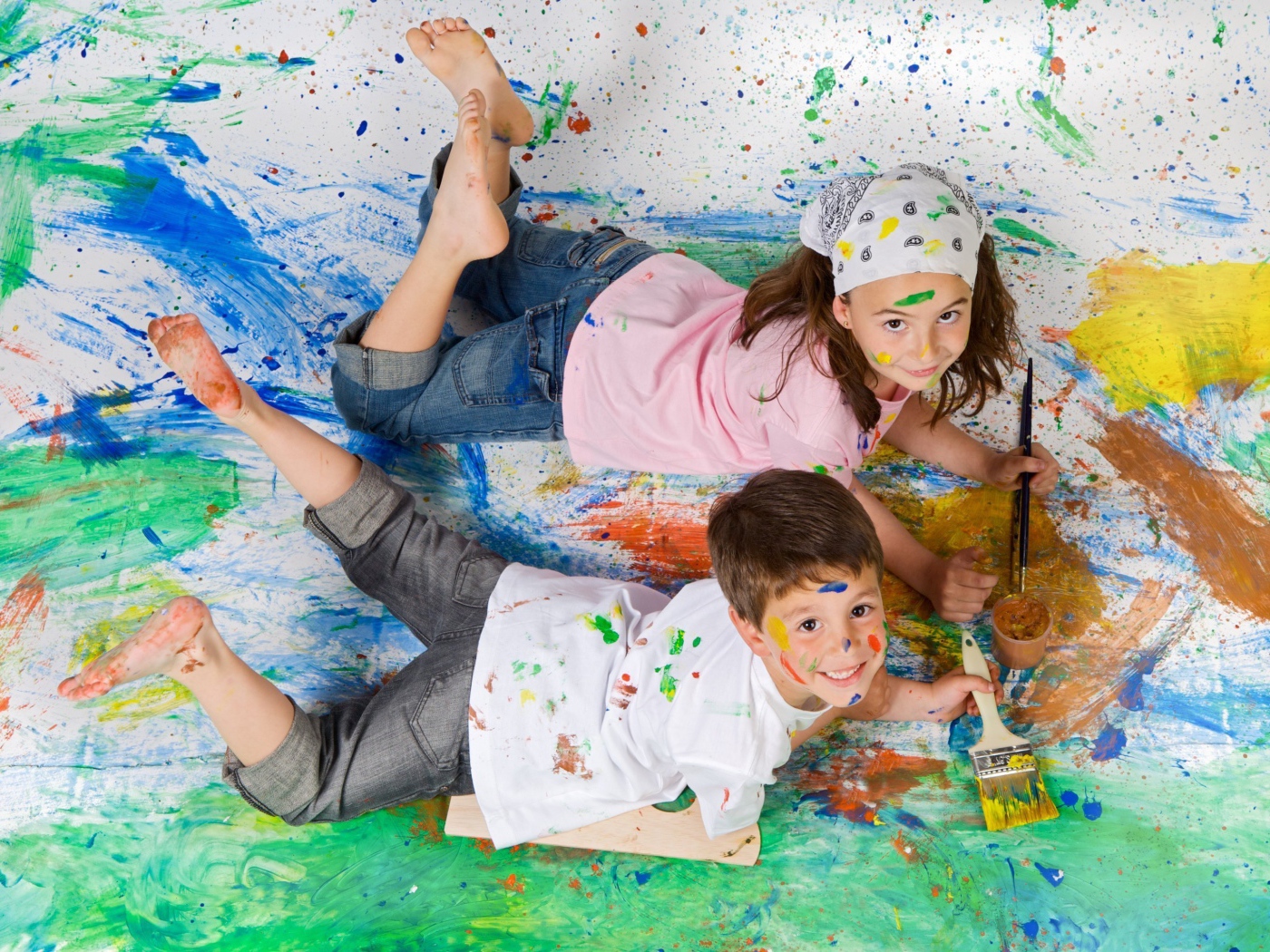 Маленькие мальчик и девочка рисуют красками на полу 