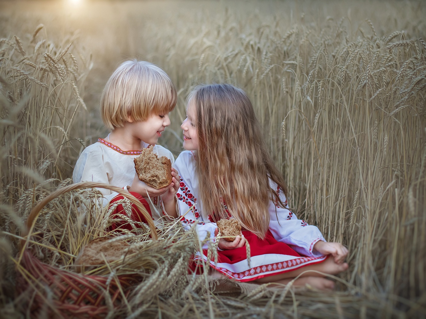 Маленькие мальчик и девочка с хлебом на пшеничном поле 