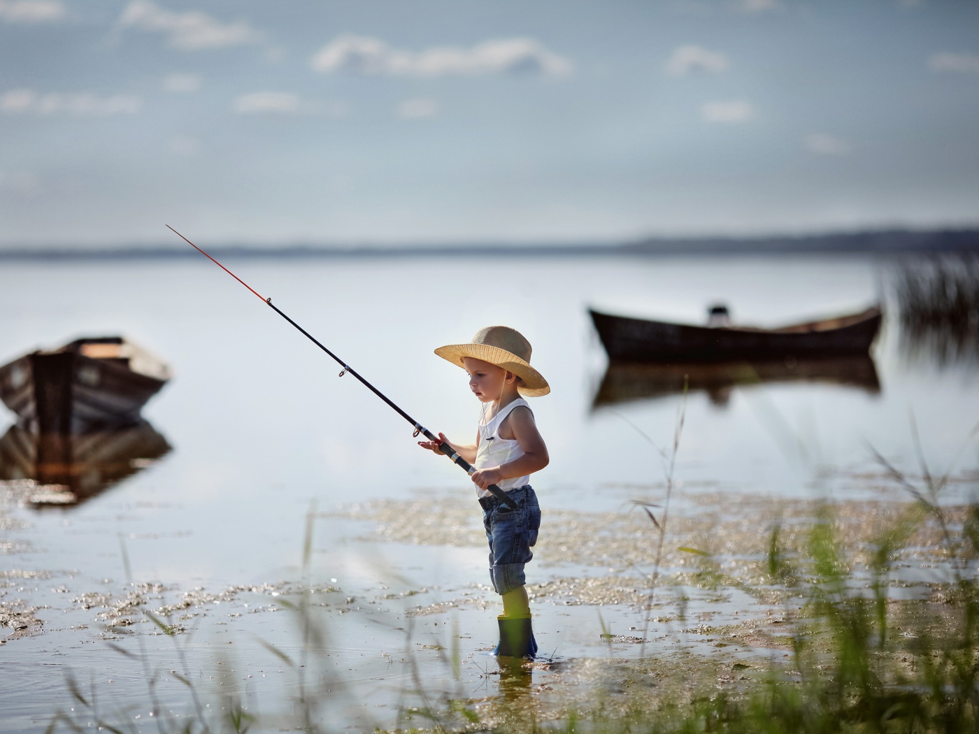 Маленький мальчик в шляпе ловит рыбу в озере 