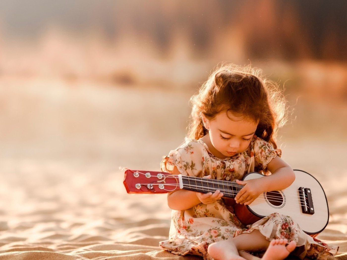 Маленькая девочка с гитарой сидит на песке 