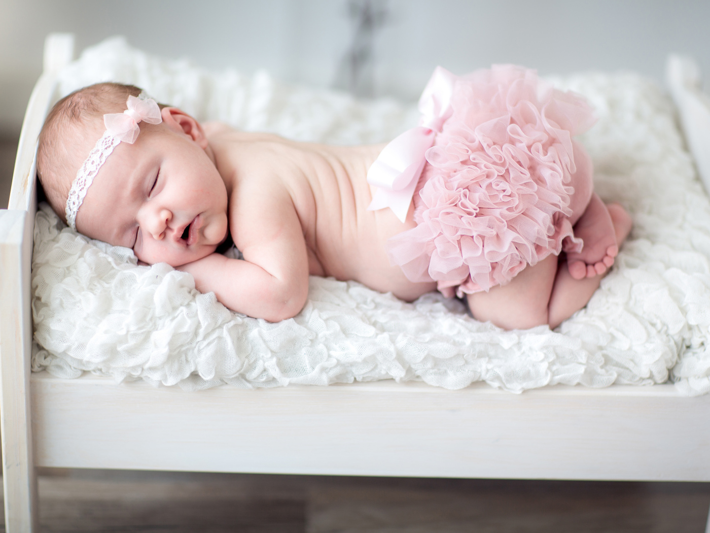 Маленькая спящая девочка в розовом костюме в кроватке