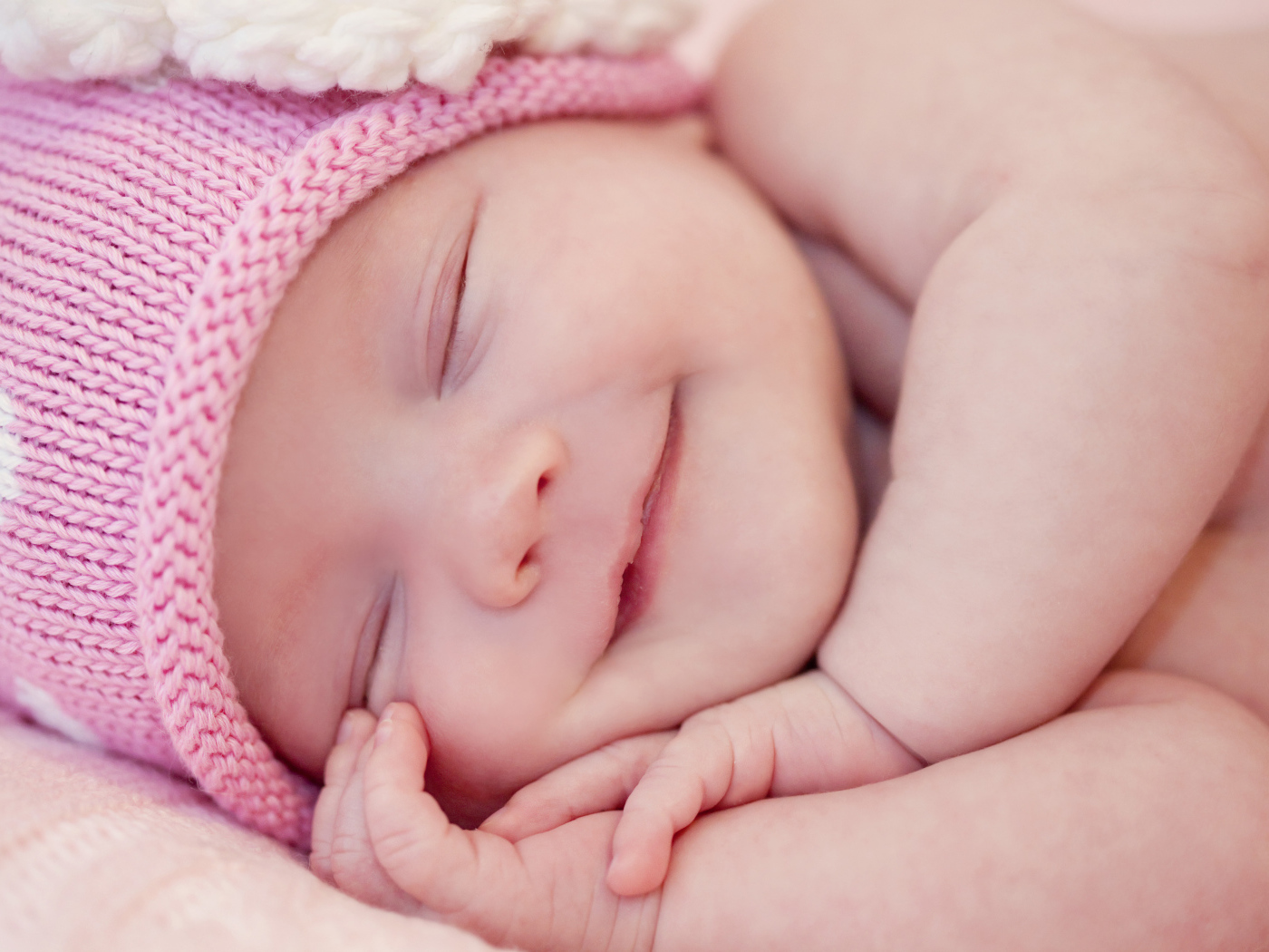 Улыбающийся грудной ребенок в розовой вязаной шапке 