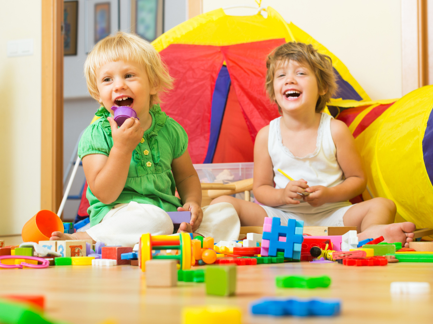 Два улыбающихся ребенка играют с конструктором 