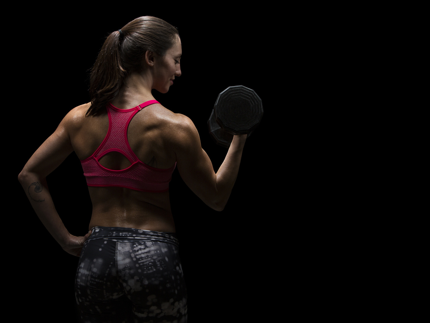 Девушка качает руки гантелей на черном фоне 