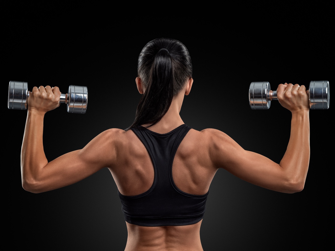 Стройная спортивная девушка с гантелями в руках на черном фоне