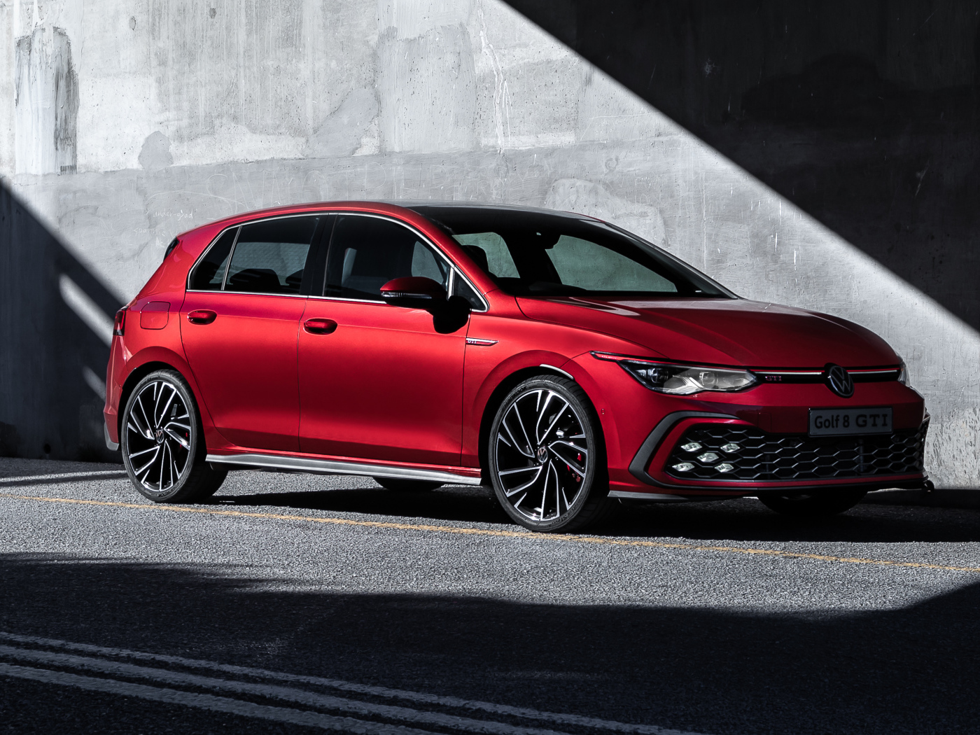 Красный автомобиль Volkswagen Golf GTI 2021 года у серой стены
